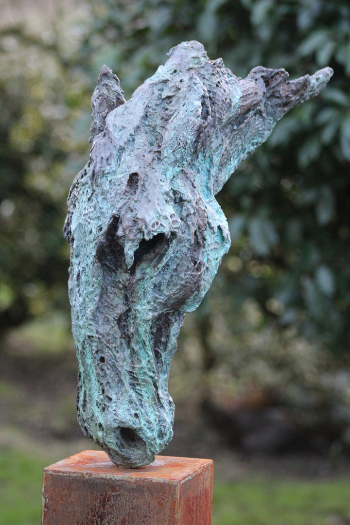 Abstract bronze sculpture of a horse’s head, mounted on a tall corten steel plinth, displayed in various garden and outdoor settings. The textured verdigris patina highlights the expressive contours and emotional form of the equine subject.
