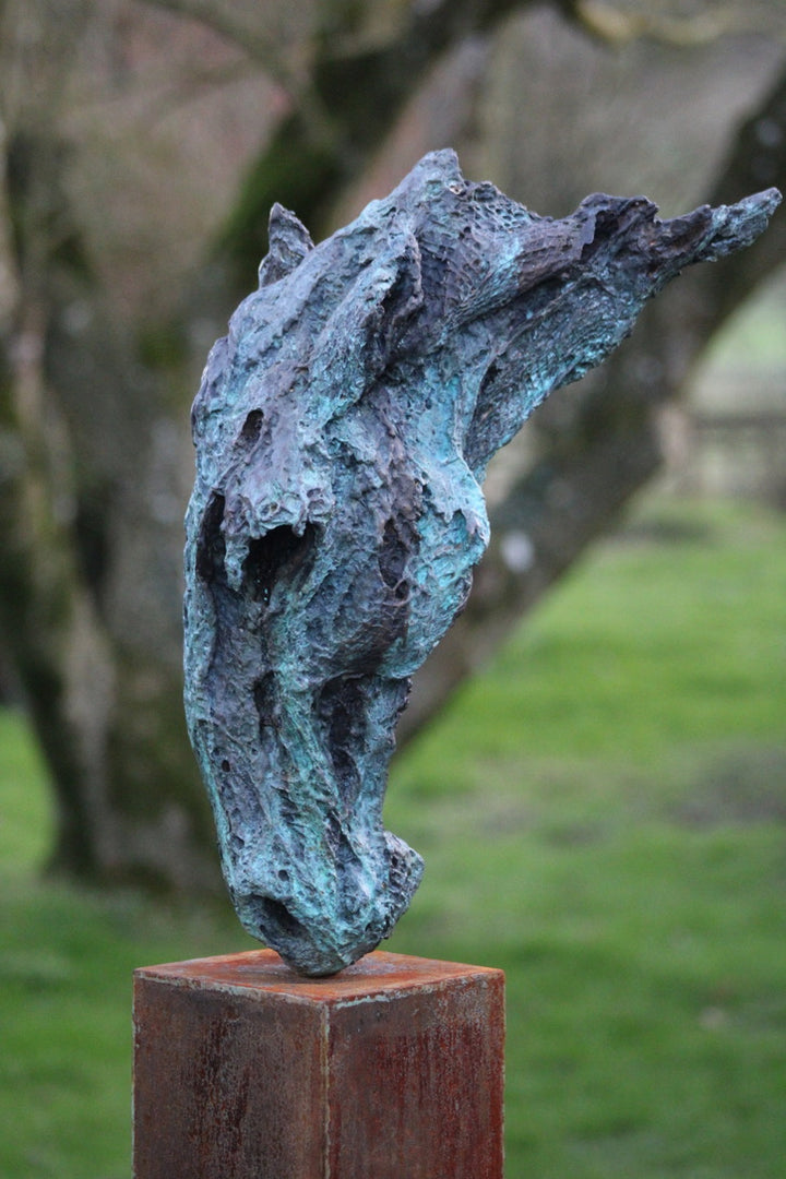 Abstract bronze sculpture of a horse’s head, mounted on a tall corten steel plinth, displayed in various garden and outdoor settings. The textured verdigris patina highlights the expressive contours and emotional form of the equine subject.