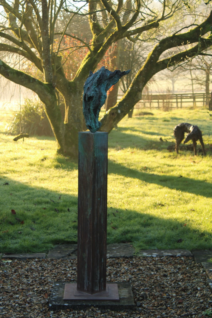 Abstract bronze sculpture of a horse’s head, mounted on a tall corten steel plinth, displayed in various garden and outdoor settings. The textured verdigris patina highlights the expressive contours and emotional form of the equine subject.
