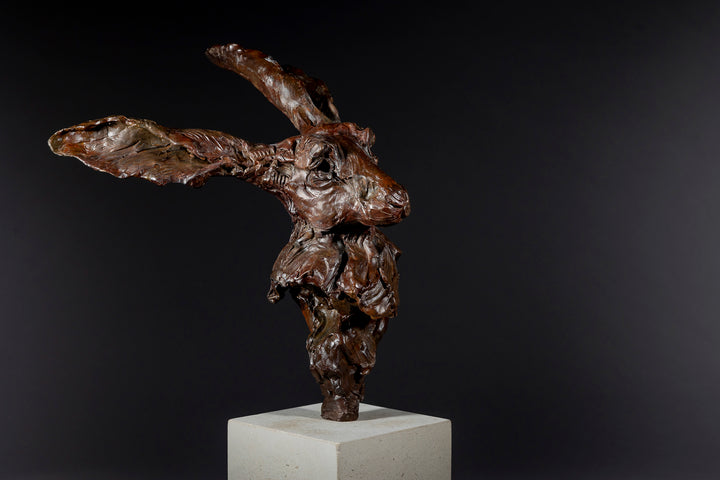 Expressive bronze sculpture of a hare’s head with exaggerated upright ears, mounted on a smooth Portland stone base.