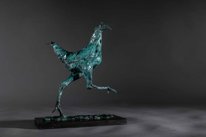 Bronze sculpture of a proud gaming cockerel mid-stride, with elongated legs and intricate feather textures, finished in a rich verdigris patina, mounted on a slate base.