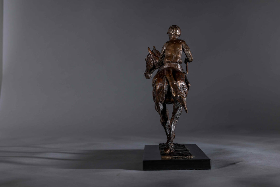 Bronze sculpture of a racehorse and jockey, titled Little White Lie, featuring a classic stance with refined detailing that captures both the poise of the rider and the strength of the thoroughbred. Mounted on a dark slate base, presented against a grey studio background.