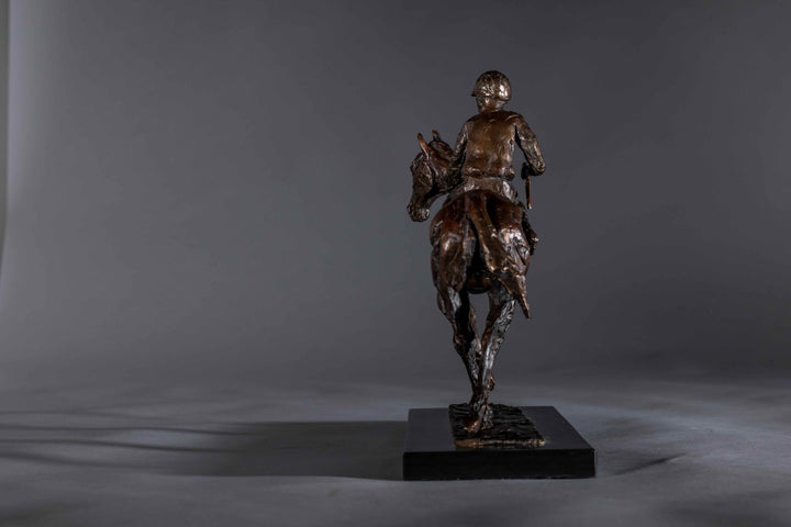 Bronze sculpture of a racehorse and jockey, titled Little White Lie, featuring a classic stance with refined detailing that captures both the poise of the rider and the strength of the thoroughbred. Mounted on a dark slate base, presented against a grey studio background.