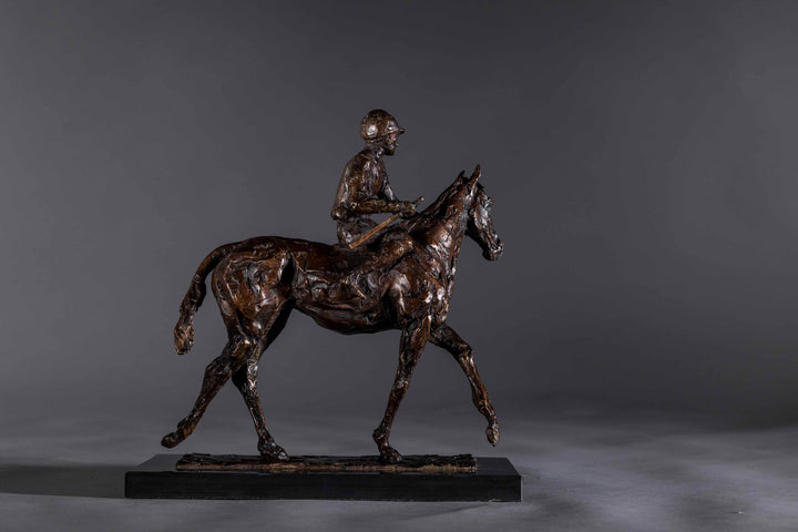 Bronze sculpture of a racehorse and jockey, titled Little White Lie, featuring a classic stance with refined detailing that captures both the poise of the rider and the strength of the thoroughbred. Mounted on a dark slate base, presented against a grey studio background.