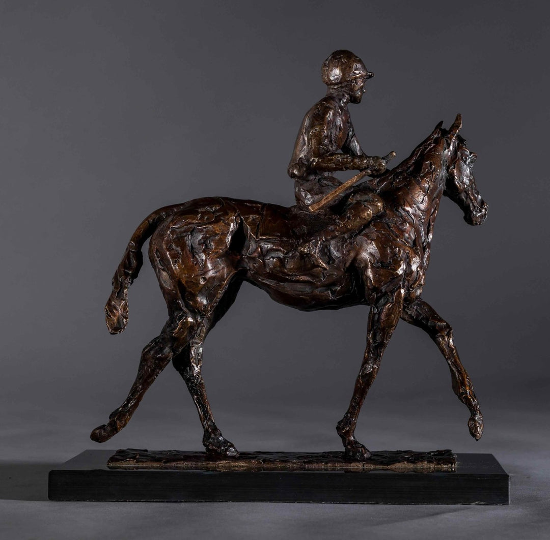 Bronze sculpture of a racehorse and jockey, titled Little White Lie, featuring a classic stance with refined detailing that captures both the poise of the rider and the strength of the thoroughbred. Mounted on a dark slate base, presented against a grey studio background.