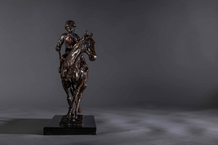 Bronze sculpture of a racehorse and jockey, titled Little White Lie, featuring a classic stance with refined detailing that captures both the poise of the rider and the strength of the thoroughbred. Mounted on a dark slate base, presented against a grey studio background.