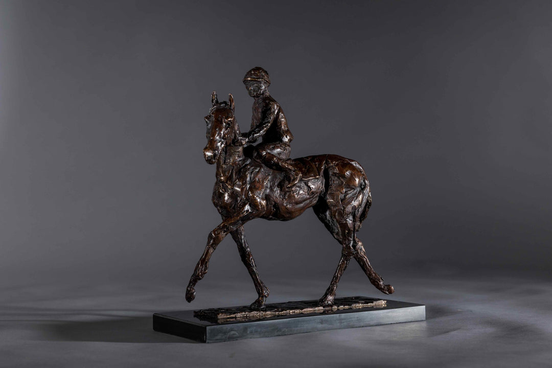 Bronze sculpture of a racehorse and jockey, titled Little White Lie, featuring a classic stance with refined detailing that captures both the poise of the rider and the strength of the thoroughbred. Mounted on a dark slate base, presented against a grey studio background.