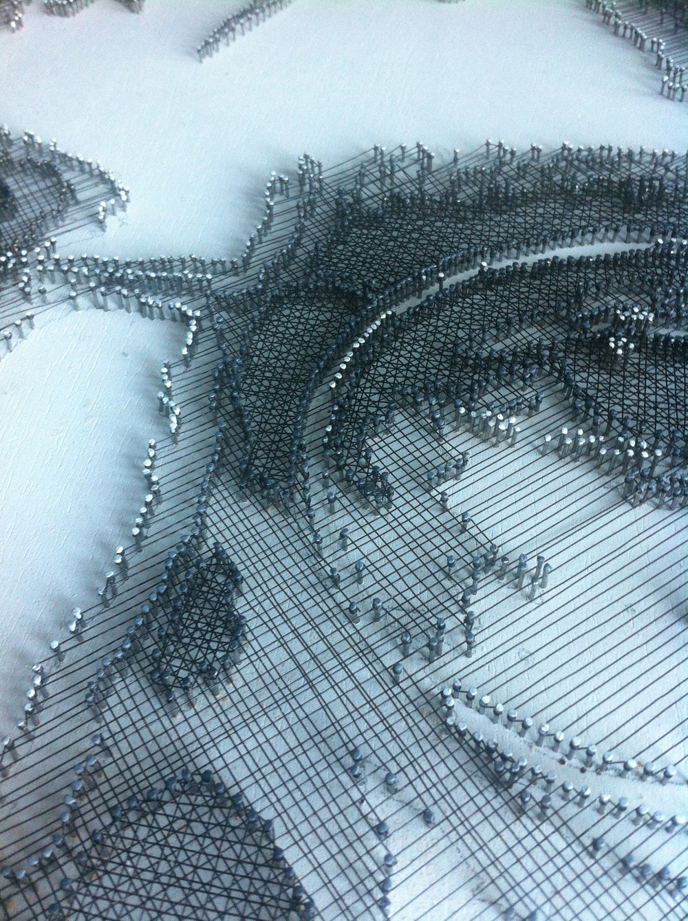 Portrait of John Lennon formed from fine black enamelled copper wire tensioned around thousands of small nails on a white board, with layered linear wiring defining facial features, round glasses and hair through tonal contrast, depth and shadow across a textured monochrome surface.