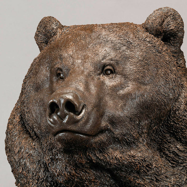 Large bronze head study of a Kodiak brown bear by Nick Bibby, showing powerful form, dense textured fur and rich brown patina, mounted on a tall bronze plinth with mottled green and earthy tones.