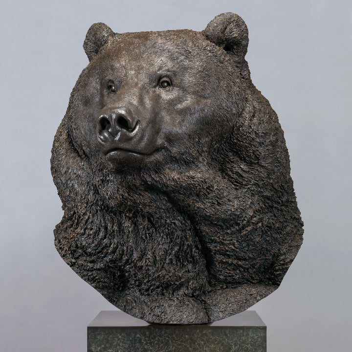 Large bronze head study of a Kodiak brown bear by Nick Bibby, showing powerful form, dense textured fur and rich brown patina, mounted on a tall bronze plinth with mottled green and earthy tones.