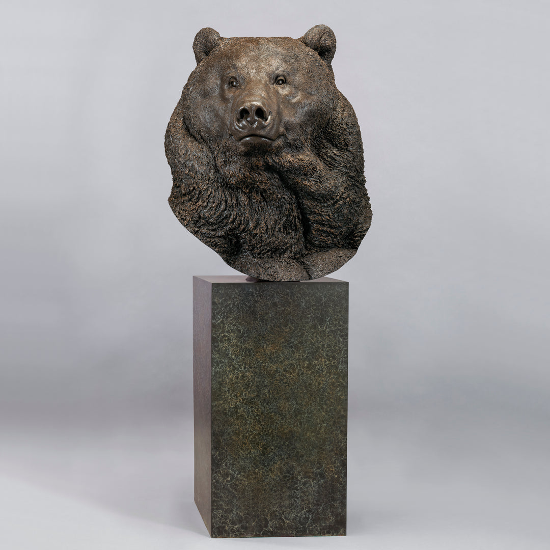Large bronze head study of a Kodiak brown bear by Nick Bibby, showing powerful form, dense textured fur and rich brown patina, mounted on a tall bronze plinth with mottled green and earthy tones.