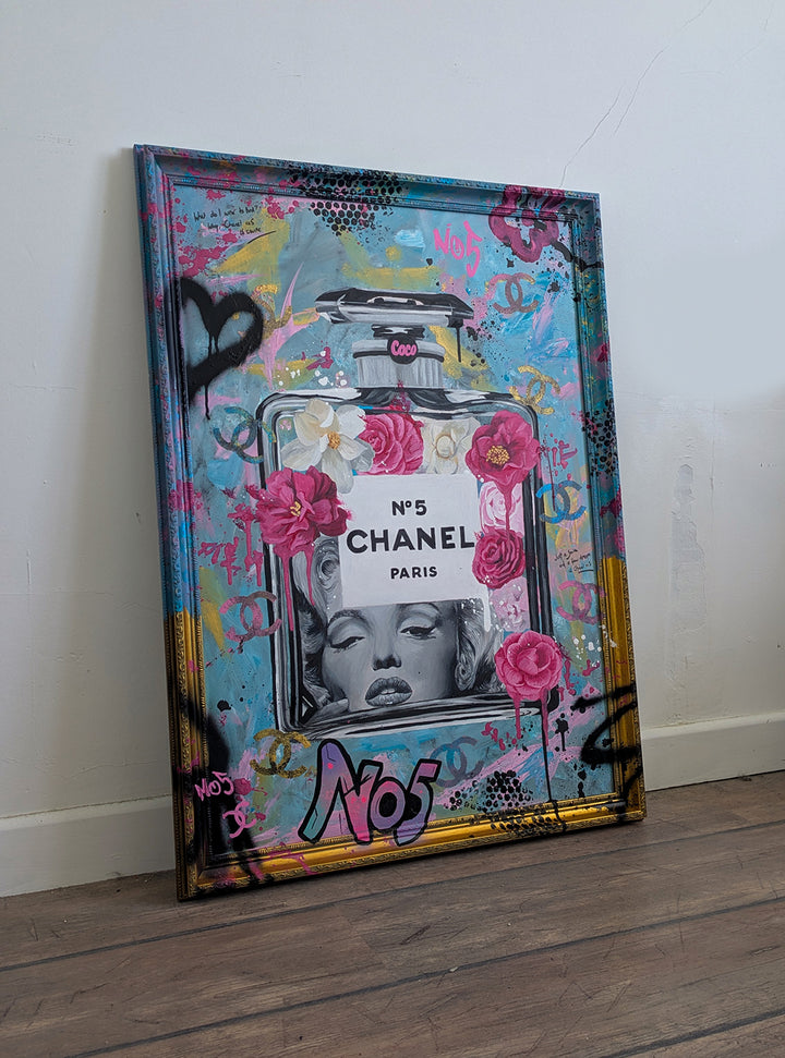 "Marilyn Monroe X Chanel No.5" – a bold embellished art print by Ian Salmon, featuring a black-and-white portrait of Marilyn Monroe embedded in a painted Chanel No.5 bottle, surrounded by vivid pink and red Camellia flowers, graffiti-style branding, and set against a turquoise, pastel blue, and gold accented background with a hand-painted custom frame.