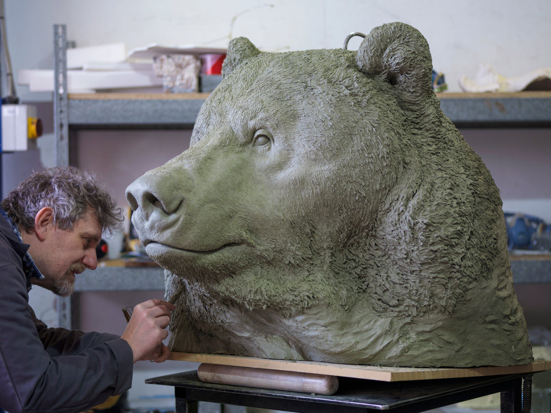 Large bronze head study of a Kodiak brown bear by Nick Bibby, showing powerful form, dense textured fur and rich brown patina, mounted on a tall bronze plinth with mottled green and earthy tones.