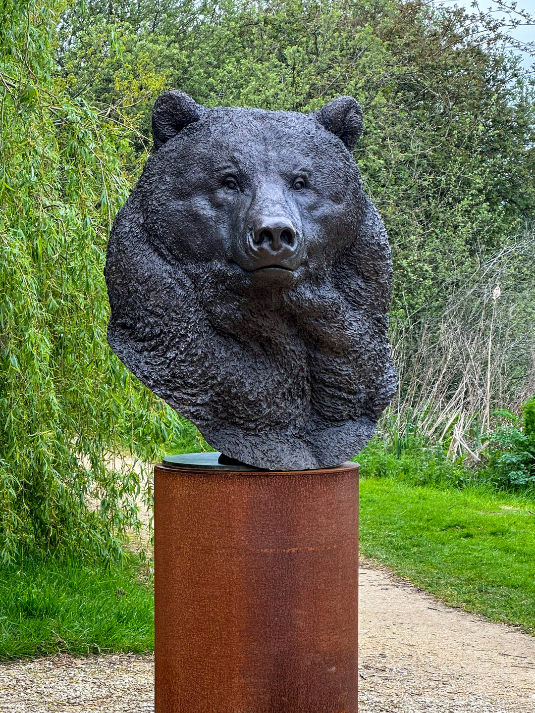 Large bronze head study of a Kodiak brown bear by Nick Bibby, showing powerful form, dense textured fur and rich brown patina, mounted on a tall bronze plinth with mottled green and earthy tones.