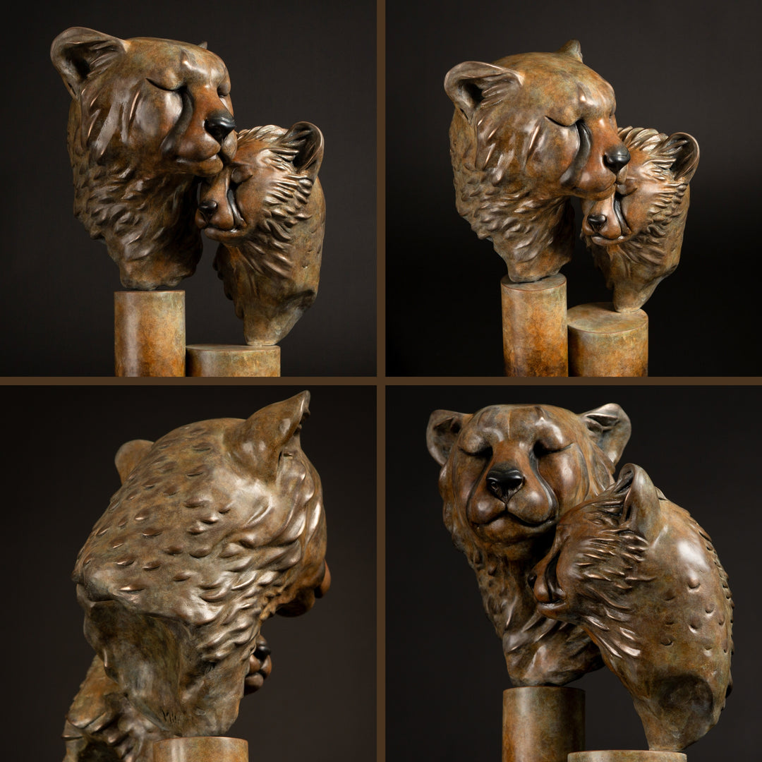 Kulina cheetah mother and cub bronze sculpture by Min Reid, tender wildlife sculpture showing a protective cheetah nuzzling her cub, warm golden brown bronze patina mounted on tall cylindrical bronze plinths against a dark background