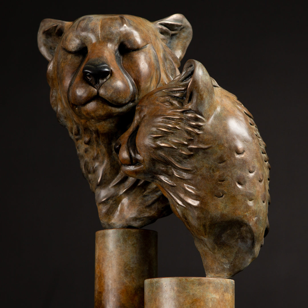 Kulina cheetah mother and cub bronze sculpture by Min Reid, tender wildlife sculpture showing a protective cheetah nuzzling her cub, warm golden brown bronze patina mounted on tall cylindrical bronze plinths against a dark background