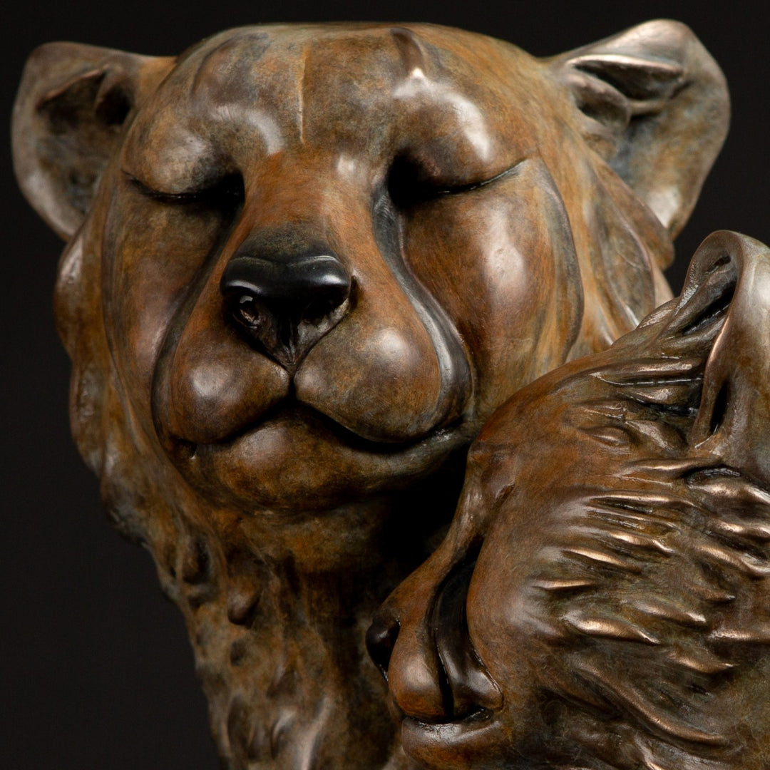 Kulina cheetah mother and cub bronze sculpture by Min Reid, tender wildlife sculpture showing a protective cheetah nuzzling her cub, warm golden brown bronze patina mounted on tall cylindrical bronze plinths against a dark background