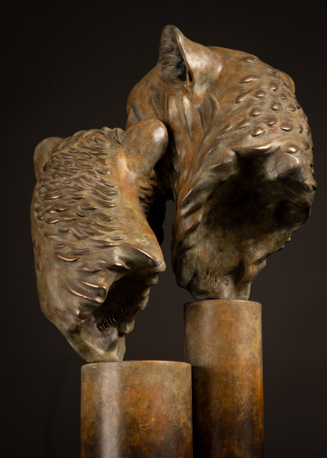 Kulina cheetah mother and cub bronze sculpture by Min Reid, tender wildlife sculpture showing a protective cheetah nuzzling her cub, warm golden brown bronze patina mounted on tall cylindrical bronze plinths against a dark background