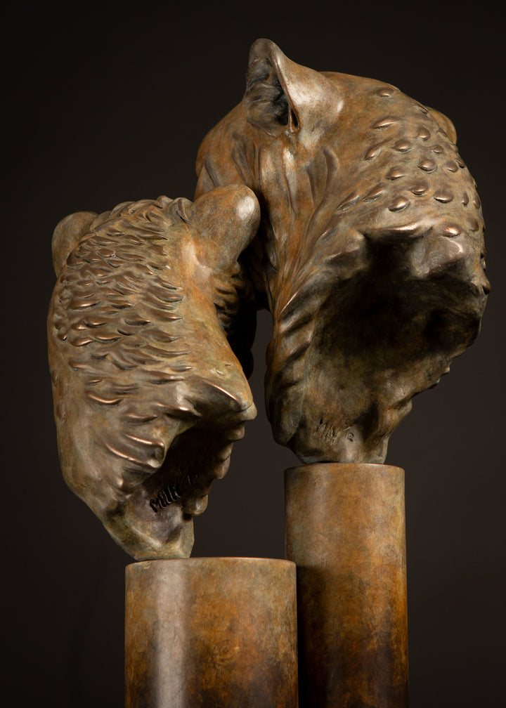 Kulina cheetah mother and cub bronze sculpture by Min Reid, tender wildlife sculpture showing a protective cheetah nuzzling her cub, warm golden brown bronze patina mounted on tall cylindrical bronze plinths against a dark background