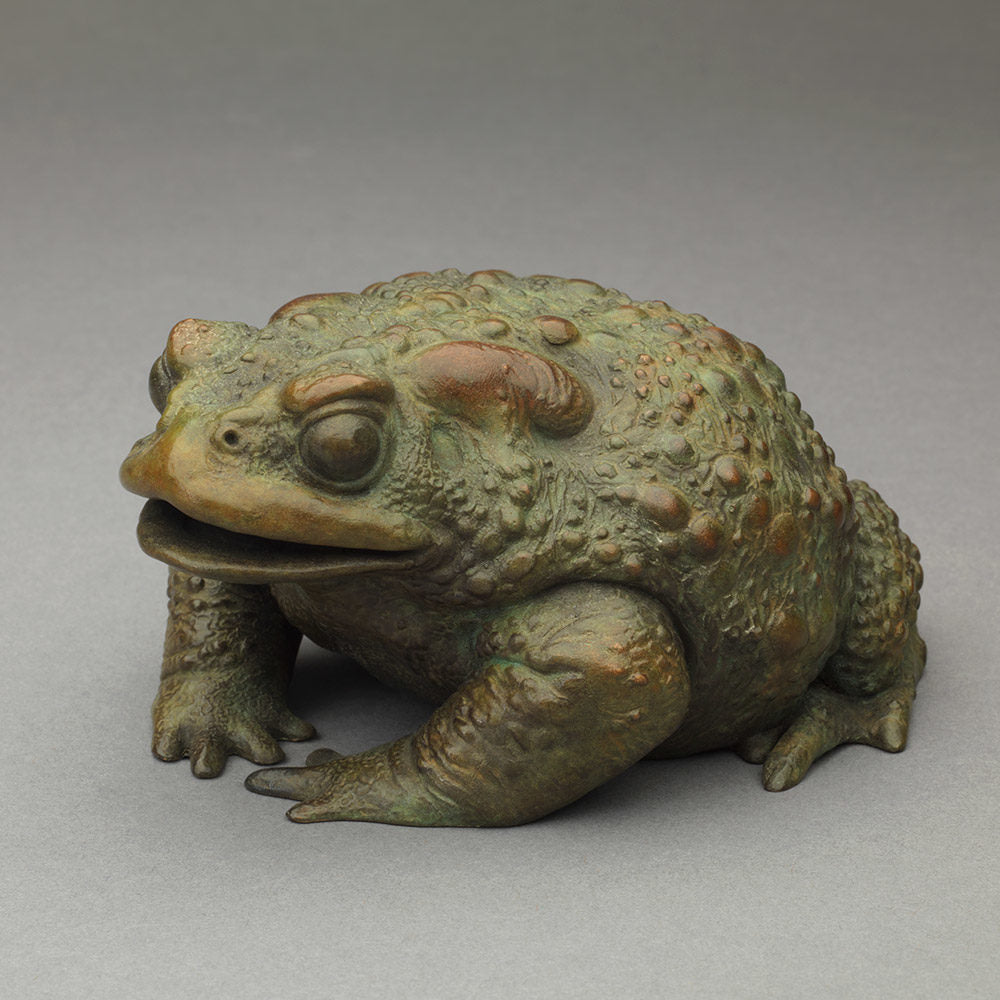 Bronze sculpture of a small toad in a seated, alert posture, detailed textured skin with raised bumps and a natural green–bronze patina.