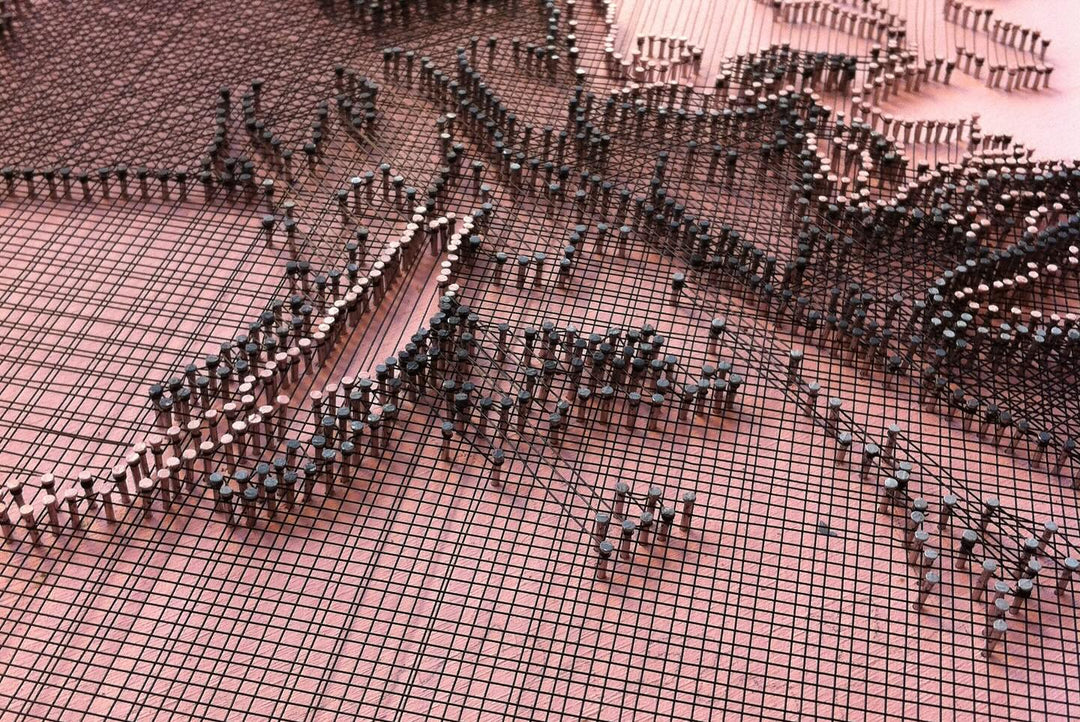 Portrait of Lady Gaga constructed from fine copper wire tensioned around numerous small nails on a painted board, with layered linear wiring forming facial features, hair and hat through tonal variation, depth and shadow across a textured pink-toned surface.