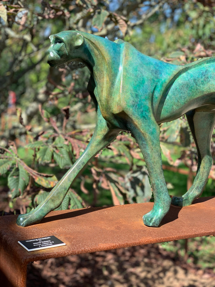 Marie Ackers The Walking Cheetah bronze sculpture in verdigris green patina, limited edition of 8. Stylised cheetah mid-stride, long tail extended, capturing elegance, rhythm, and the essence of feline movement in contemporary bronze.