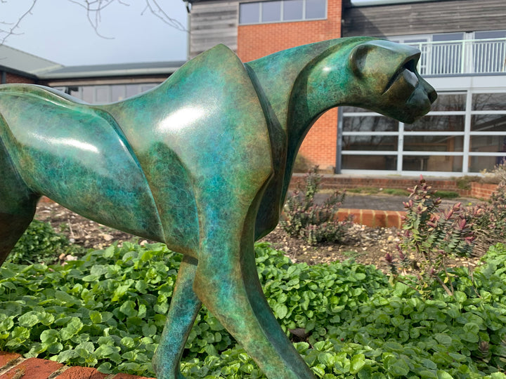 Marie Ackers The Walking Cheetah bronze sculpture in verdigris green patina, limited edition of 8. Stylised cheetah mid-stride, long tail extended, capturing elegance, rhythm, and the essence of feline movement in contemporary bronze.