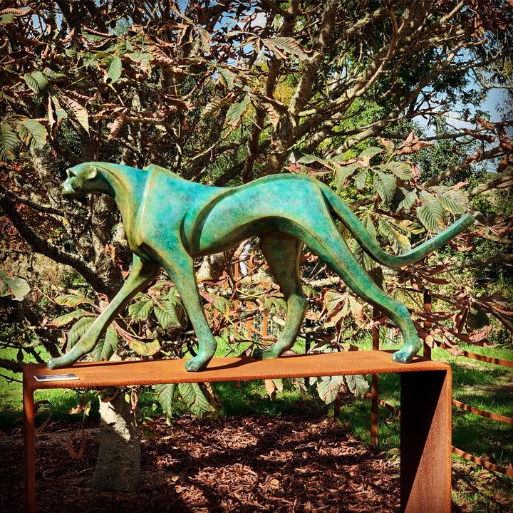Marie Ackers The Walking Cheetah bronze sculpture in verdigris green patina, limited edition of 8. Stylised cheetah mid-stride, long tail extended, capturing elegance, rhythm, and the essence of feline movement in contemporary bronze.