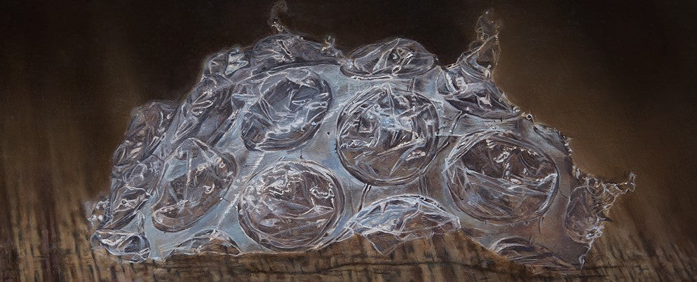 Simon Taylor, Left Behind, 2024, oil on canvas, 17 x 41cm – photorealist painting of a torn fragment of clear bubble wrap resting on a dark wooden surface, with detailed translucent pockets and soft reflections in warm brown light.