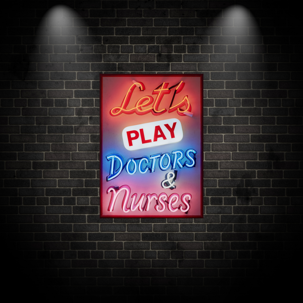 A vibrant neon sign artwork by Matthew Bracey reading “Let’s Play Doctors & Nurses.” The piece features glowing script and block fonts in red, white, blue, and pink neon set against a dark framed background, combining retro humour with bold visual impact.
