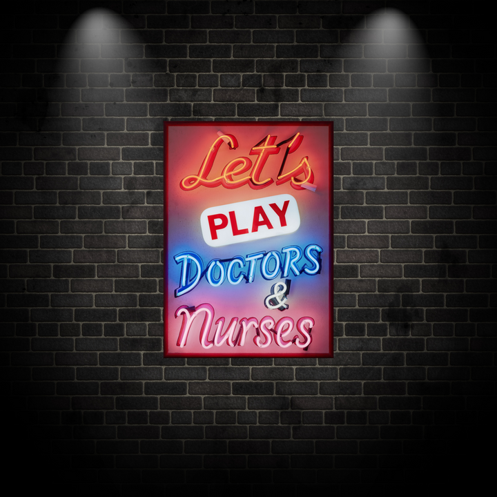 A vibrant neon sign artwork by Matthew Bracey reading “Let’s Play Doctors & Nurses.” The piece features glowing script and block fonts in red, white, blue, and pink neon set against a dark framed background, combining retro humour with bold visual impact.