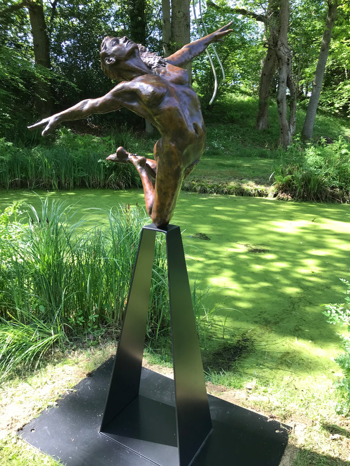 Teresa Wells’ bronze sculpture Liberty (2019), limited edition of 12, depicting a nude female figure in a dynamic leap with arms and head thrown back, one leg extended and the other bent mid-air. Cast in warm patinated bronze and mounted on a tall, powder-coated steel plinth, the piece balances elegance, athleticism, and expressive movement. At 98cm × 60cm × 190cm and 95kg, it is suited for both interior display and sheltered outdoor settings, with fine anatomical detailing smooth contours.