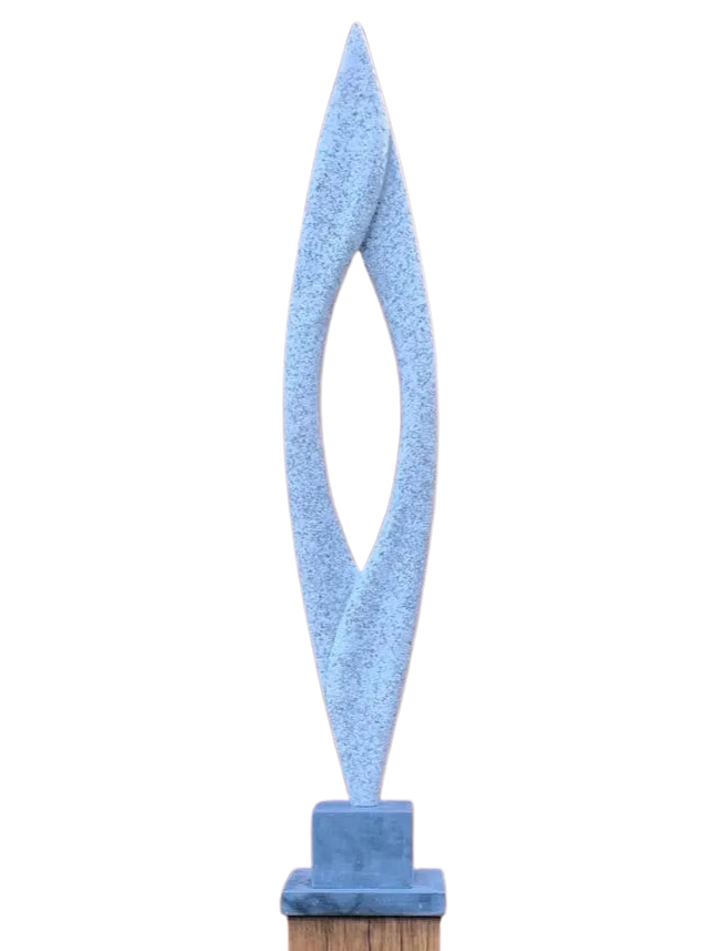 Abstract sculpture Lighthouse – 2024 by Hamish Holman, carved from Cornish granite into a tall, slender vertical form with a central opening and twisting contours, mounted on a dark stone base and oak plinth, displayed outdoors in natural light.
