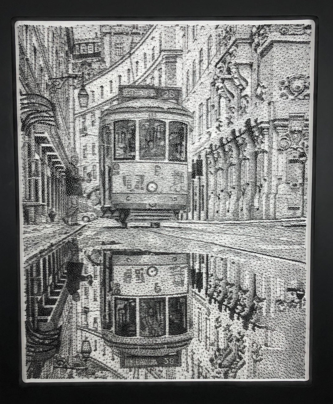 Intricate monochrome nail and string artwork of a Lisbon tram gliding through a historic street, with its reflection perfectly mirrored in a wet cobbled road.