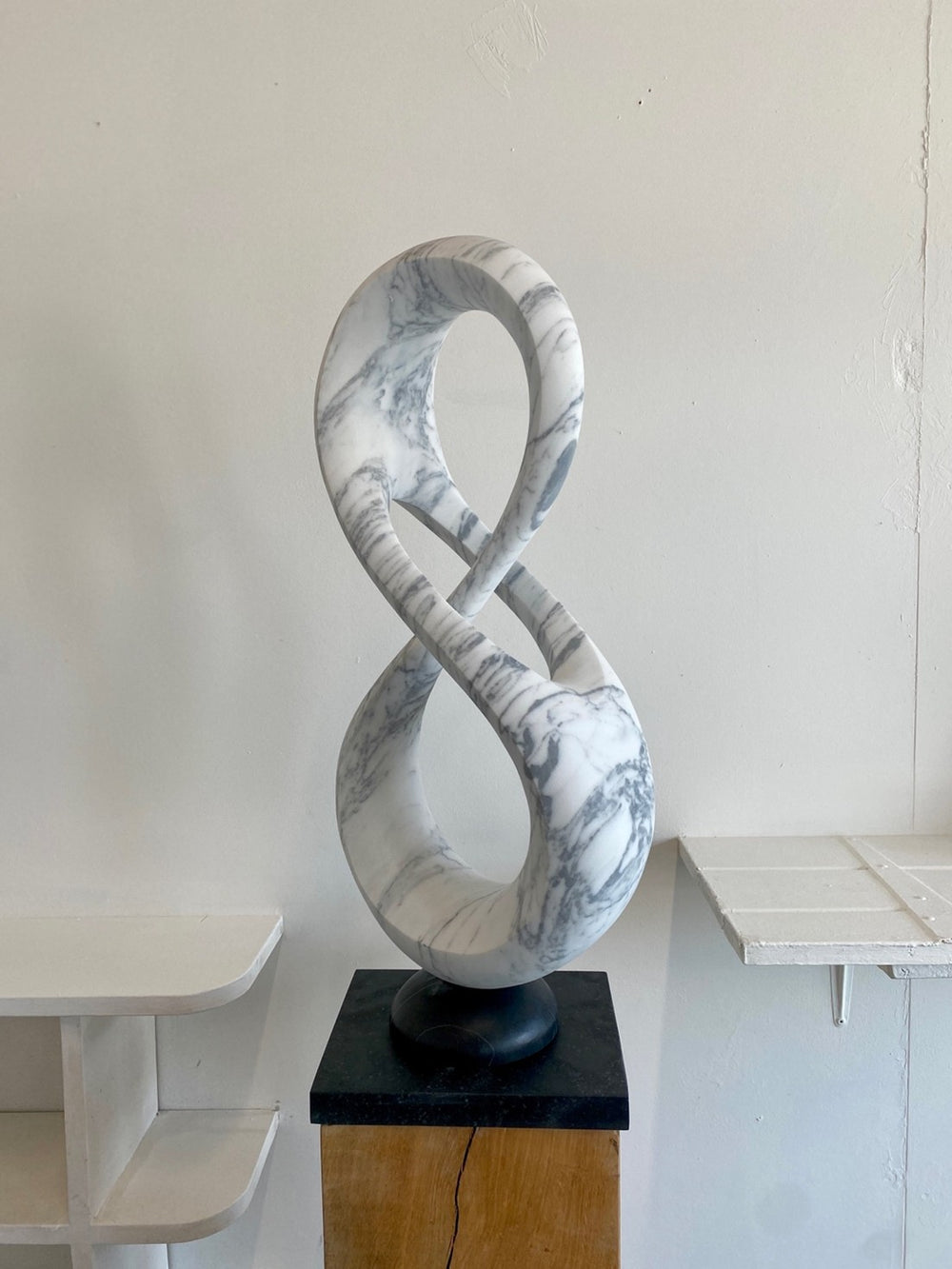 Abstract marble sculpture Loopdreams – 2025 by Hamish Holman, carved from Venatino marble into an elegant looping infinity-inspired form with flowing curves and open voids, set on a dark stone base and oak plinth.