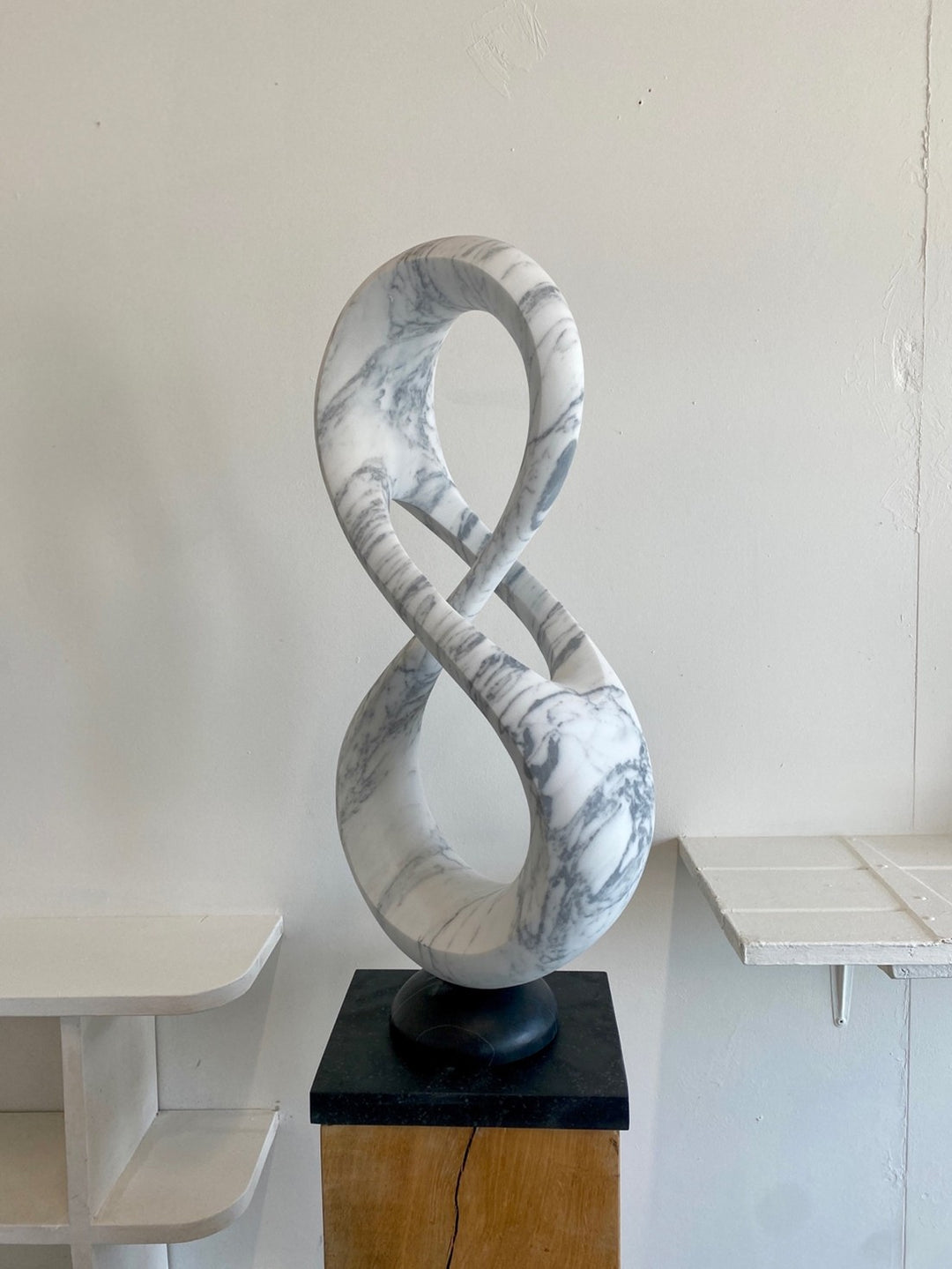 Abstract marble sculpture Loopdreams – 2025 by Hamish Holman, carved from Venatino marble into an elegant looping infinity-inspired form with flowing curves and open voids, set on a dark stone base and oak plinth.