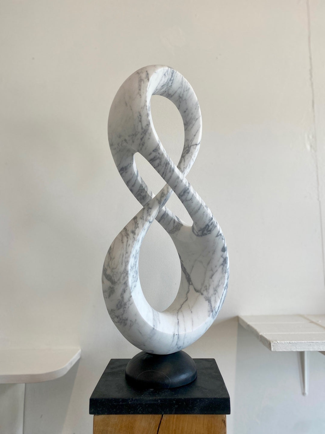 Abstract marble sculpture Loopdreams – 2025 by Hamish Holman, carved from Venatino marble into an elegant looping infinity-inspired form with flowing curves and open voids, set on a dark stone base and oak plinth.