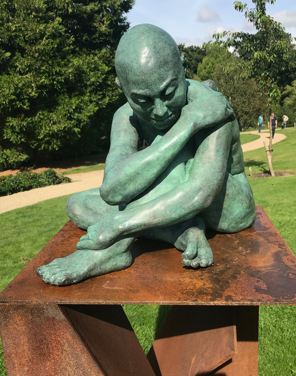 Teresa Wells’ Loss (2021), limited edition bronze sculpture, depicting a seated, nude male figure with shaved head, arms wrapped around knees in a pose of introspection and vulnerability. Finished in a rich green patina with subtle bronze undertones, the piece reveals finely modelled musculature, expressive hands and feet, and a downcast gaze. At 52cm × 42cm × 42cm and 58kg, the work conveys quiet strength and emotional depth, suitable for indoor display or sheltered outdoor placement.