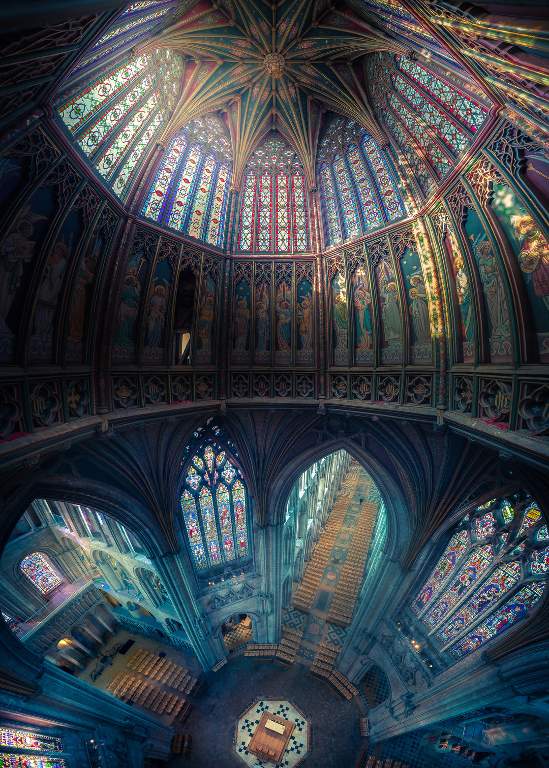 Expansive panoramic view of Ely Cathedral’s octagonal lantern tower, showing intricate stained glass, fan-vaulted roof, and painted saints, bathed in radiant light and medieval detail.
