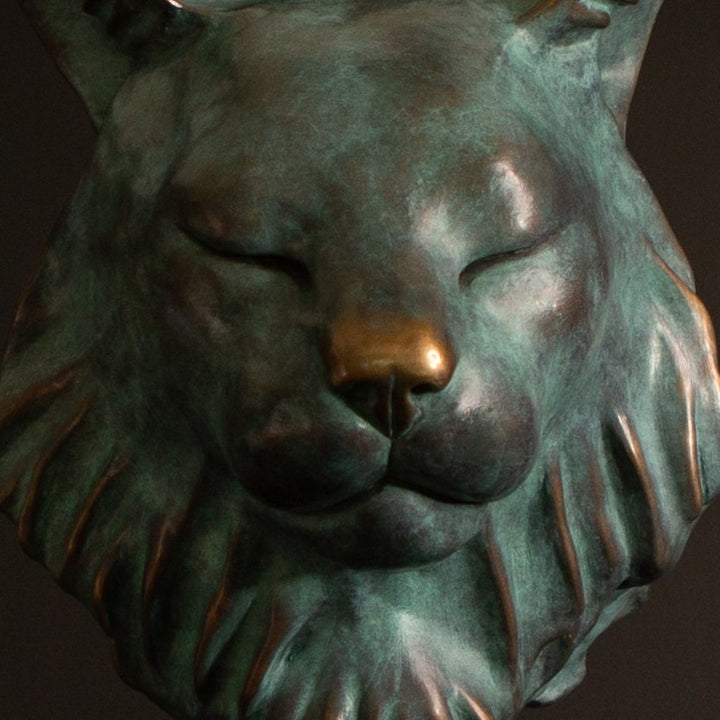 Petra Eurasian Lynx bronze sculpture by Min Reid, serene lynx head with closed eyes and pointed ear tufts in green verdigris bronze with warm copper highlights, mounted on a black plinth, contemporary wildlife bronze sculpture