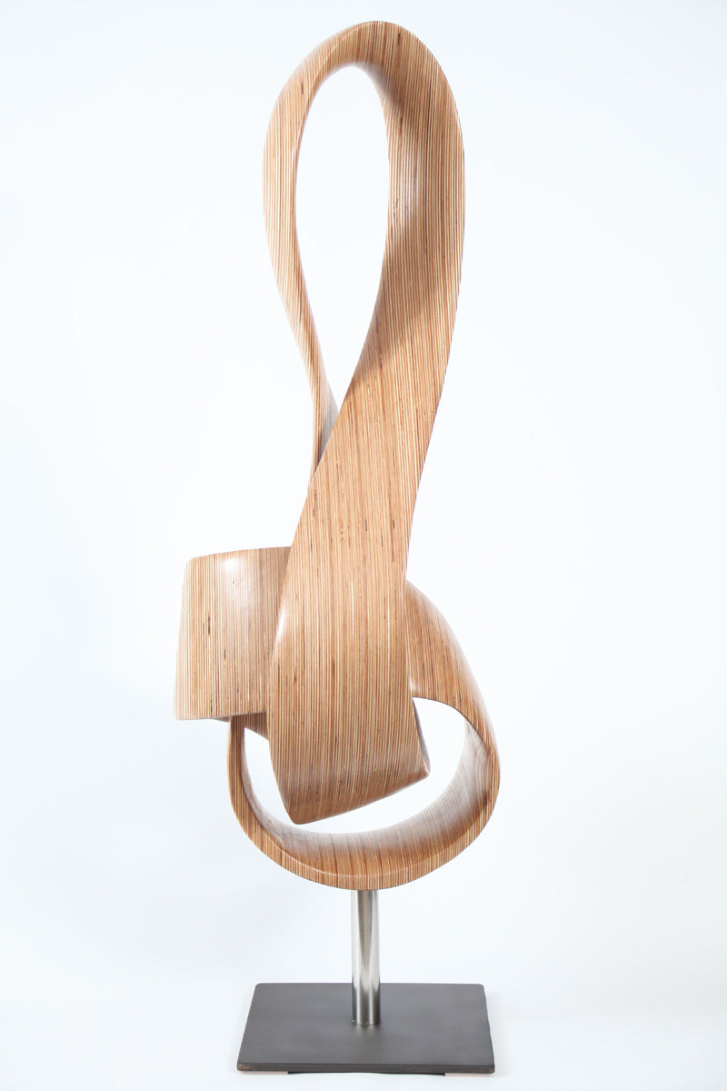 Hand-carved birch plywood sculpture by Bill Prickett combining a treble clef and Möbius strip into a continuous, flowing form, with layered wood grain revealing an infinity loop inspired by music and mathematics.