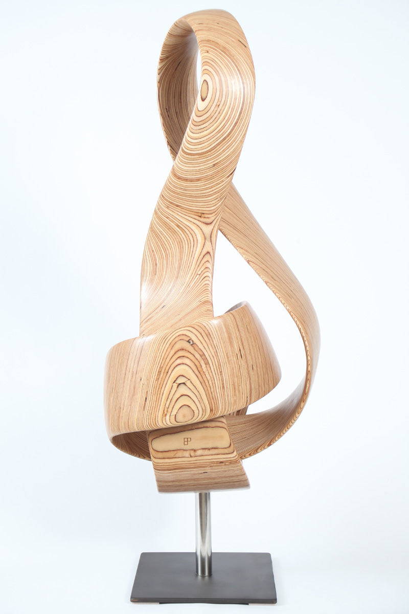 Hand-carved birch plywood sculpture by Bill Prickett combining a treble clef and Möbius strip into a continuous, flowing form, with layered wood grain revealing an infinity loop inspired by music and mathematics.