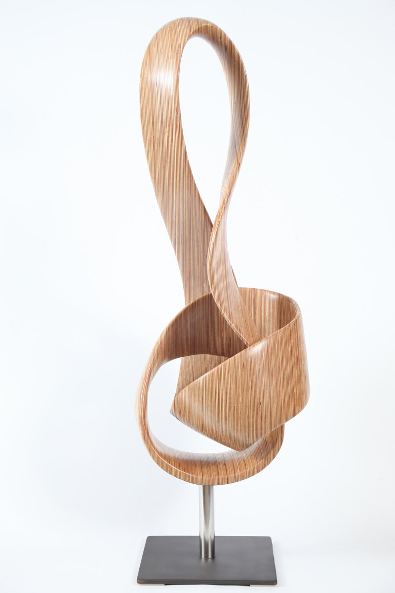 Hand-carved birch plywood sculpture by Bill Prickett combining a treble clef and Möbius strip into a continuous, flowing form, with layered wood grain revealing an infinity loop inspired by music and mathematics.