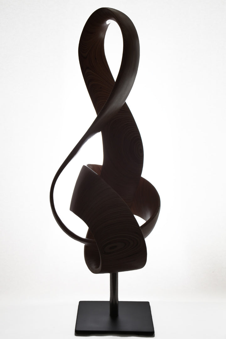 Hand-carved birch plywood sculpture by Bill Prickett combining a treble clef and Möbius strip into a continuous, flowing form, with layered wood grain revealing an infinity loop inspired by music and mathematics.