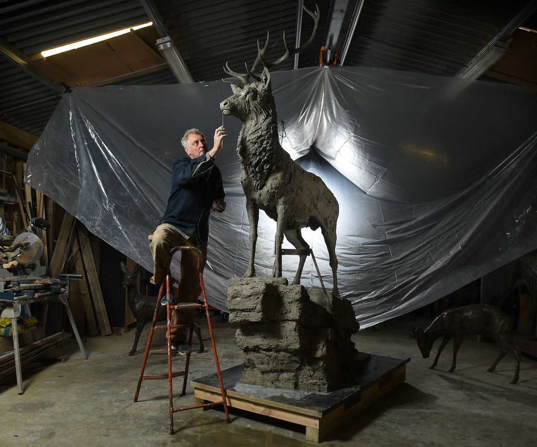 ‘Red Stag: Life Size’ by Hamish Mackie, a monumental limited-edition bronze wildlife sculpture depicting a mature Scottish Highland red deer stag standing alert on a rugged rocky outcrop. Featuring an imposing set of branching antlers, a powerful muscular body and richly textured coat, the sculpture captures the strength, dignity and commanding presence of a stag surveying its territory. Photographs show the original hand-modelled clay sculpture prior to bronze casting.