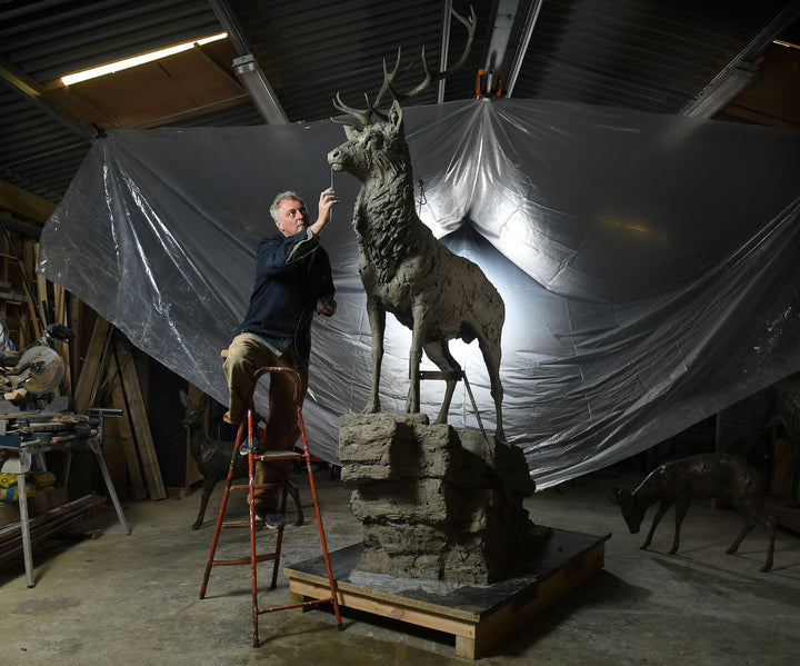 ‘Red Stag: Life Size’ by Hamish Mackie, a monumental limited-edition bronze wildlife sculpture depicting a mature Scottish Highland red deer stag standing alert on a rugged rocky outcrop. Featuring an imposing set of branching antlers, a powerful muscular body and richly textured coat, the sculpture captures the strength, dignity and commanding presence of a stag surveying its territory. Photographs show the original hand-modelled clay sculpture prior to bronze casting.