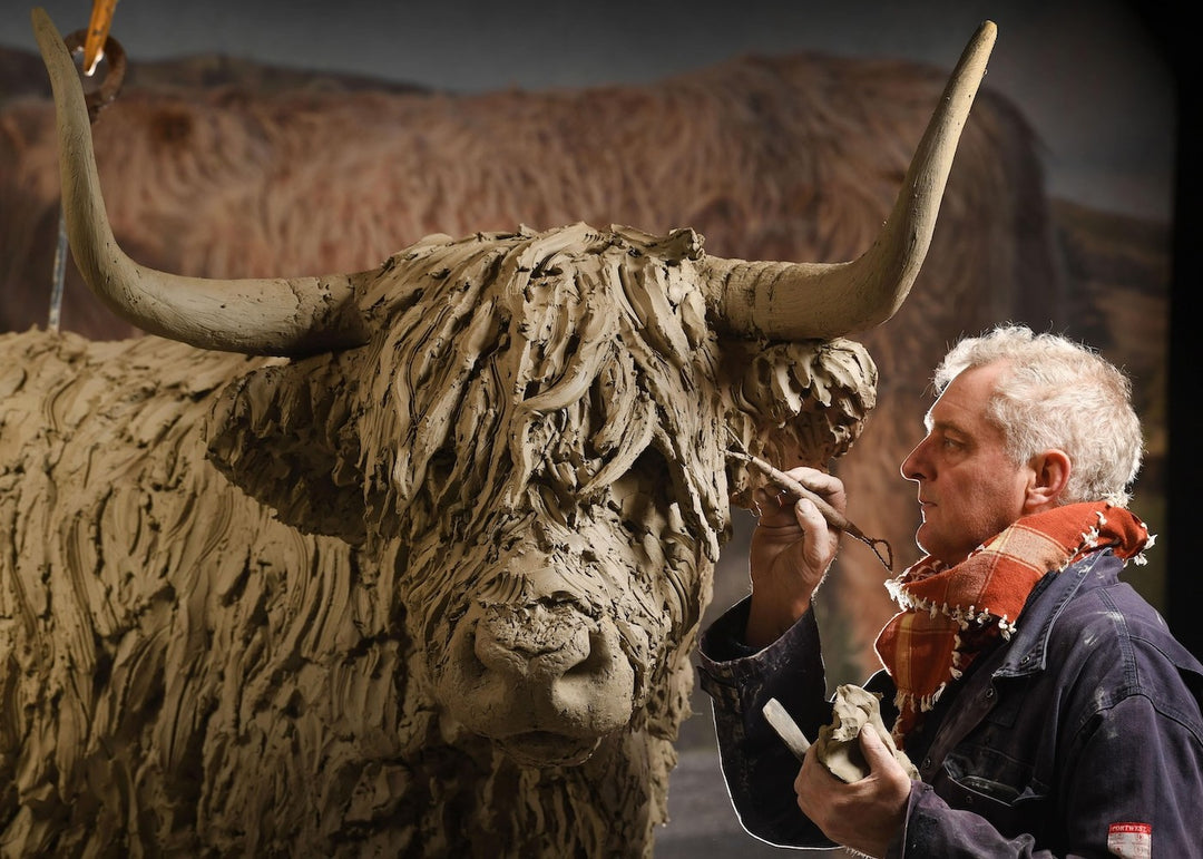 ‘Highland Cow: Life Size’ by Hamish Mackie, a life-size limited-edition bronze sculpture depicting a Scottish Highland cow standing in a grassy field. The sculpture features long, sweeping horns, a broad muzzle and a heavily textured, shaggy coat falling over the animal’s eyes. Finished in warm earthy brown bronze, the realistic wildlife sculpture captures the distinctive character and rugged appearance of the Highland breed.