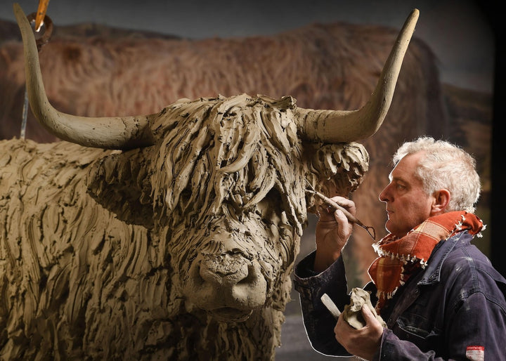 ‘Highland Cow: Life Size’ by Hamish Mackie, a life-size limited-edition bronze sculpture depicting a Scottish Highland cow standing in a grassy field. The sculpture features long, sweeping horns, a broad muzzle and a heavily textured, shaggy coat falling over the animal’s eyes. Finished in warm earthy brown bronze, the realistic wildlife sculpture captures the distinctive character and rugged appearance of the Highland breed.