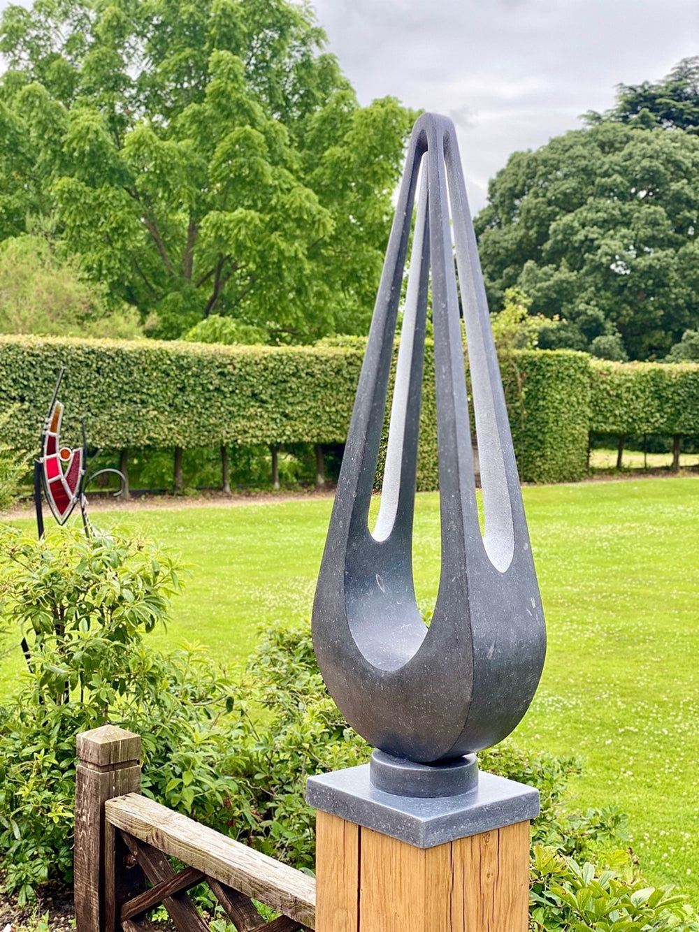Abstract sculpture Maja – 2024 by Hamish Holman, carved from dark Kilkenny limestone into a tall, teardrop-like form with elegant open voids and flowing symmetry, mounted on a stone base and oak plinth, designed for indoor or outdoor display.