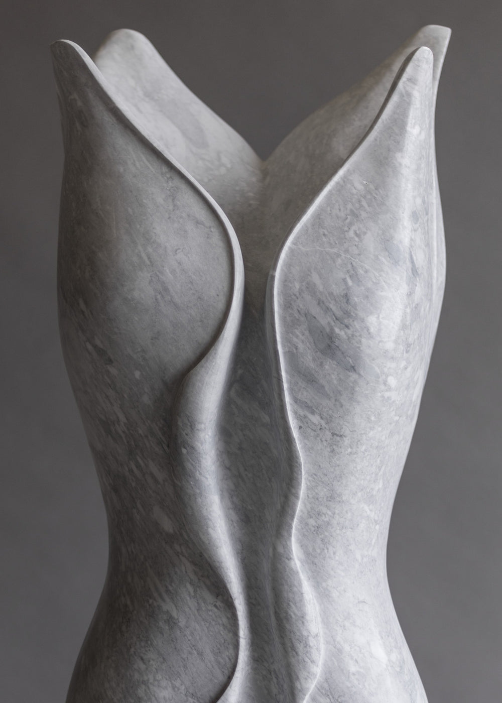 Tall contemporary sculpture hand-carved from pale Italian marble, featuring an elegant elongated form with flowing, organic curves and soft wave-like lines, poised on a smooth stone plinth with a serene, modern presence.